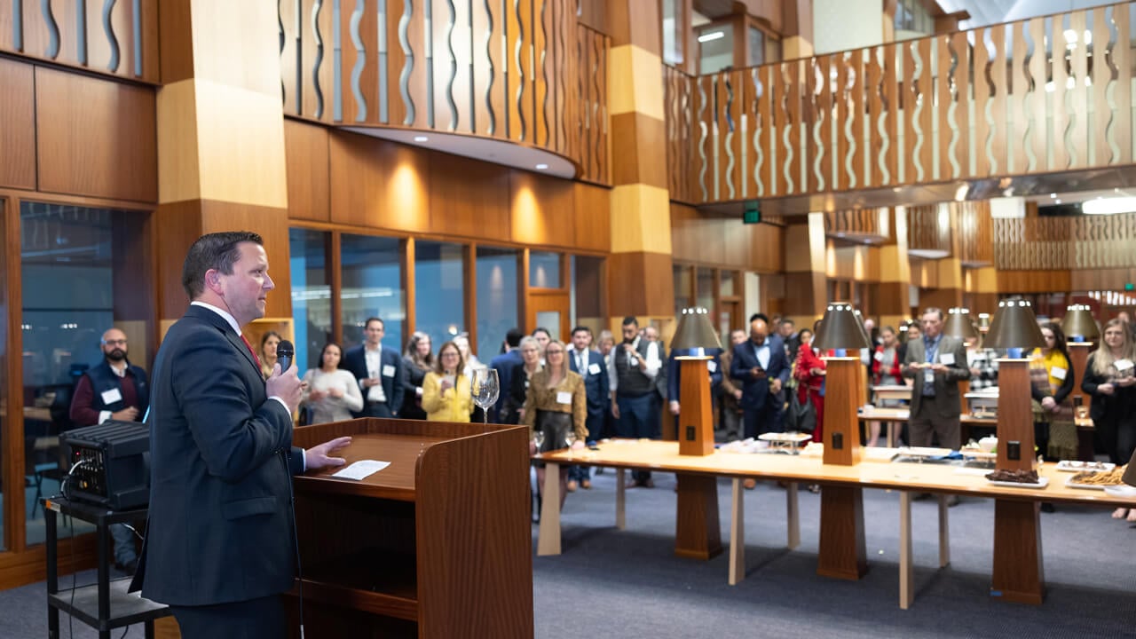 The lab library lobby is filled with event attendees while someone speaks from a podium