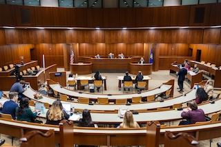 Dozens of people sit at rows of arched tables in the ceremonial courtroom