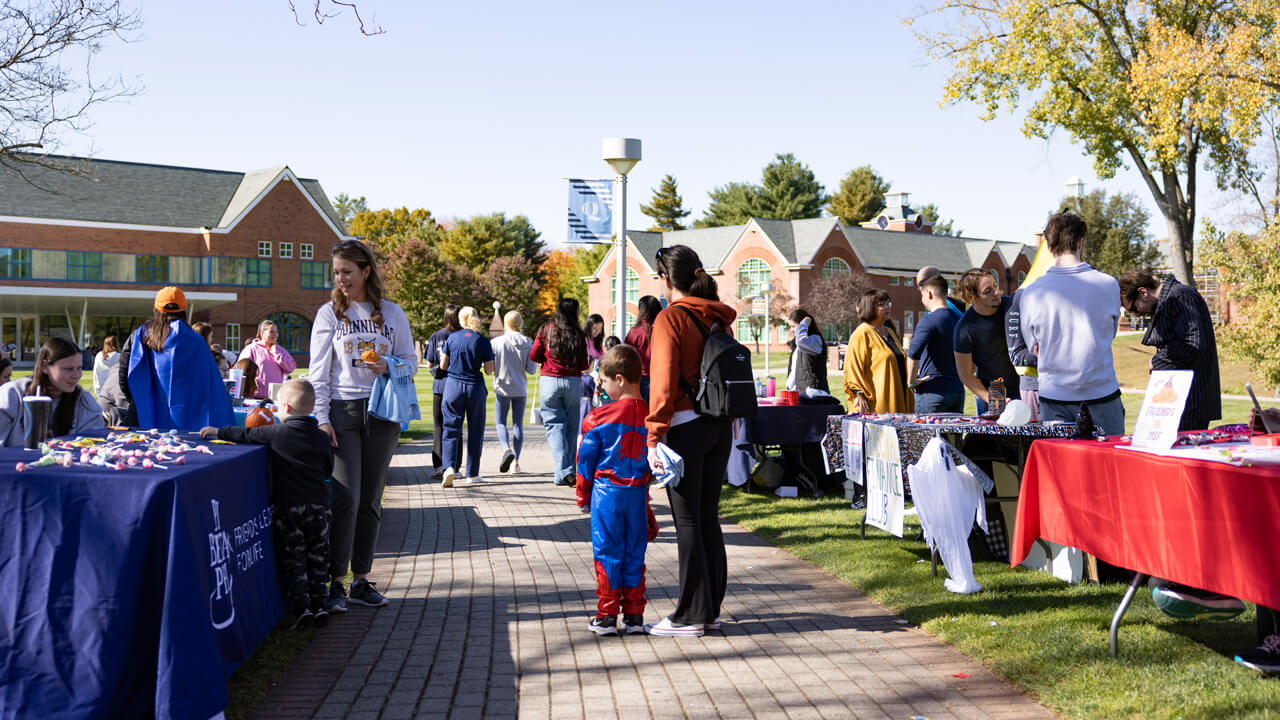 People walk amongst tables set up on the quad in a fair-like environment