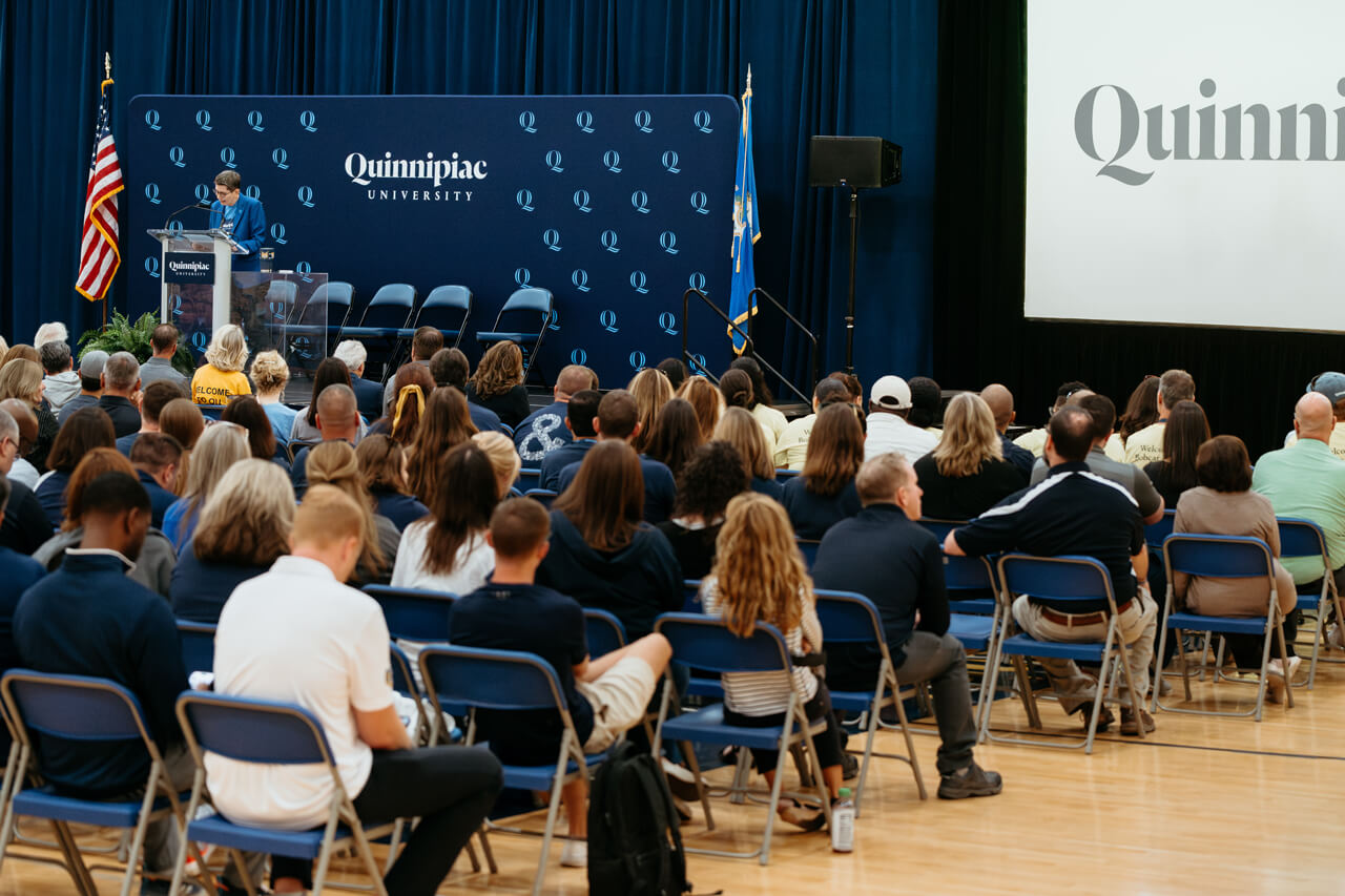 A presenter at a podium on stage in front of rows of audience members